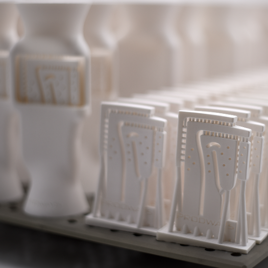 Close-up of numerous white 3D-printed industrial parts neatly arranged on a perforated build plate, showcasing production efficiency.